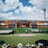 A sports stadium with a large stage set up on the field, hosting an outdoor event. Spectators wearing colorful hats sit in the foreground. The seating areas display vibrant colors, and a clear blue sky with scattered clouds is visible. Large screens display graphics related to the event.